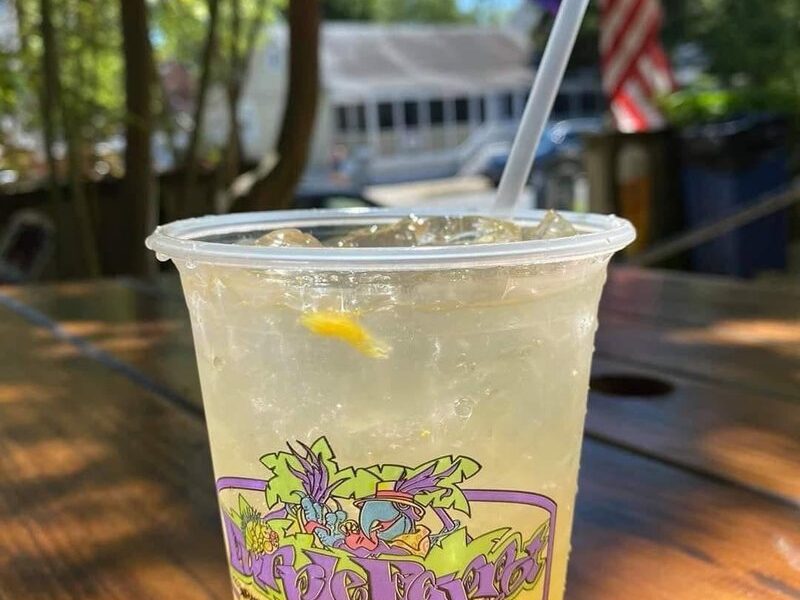A cold drink in a Purple Parrot Grill cup on a sunny biergarten table
