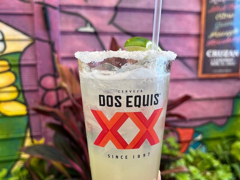 A salt-rimmed margarita in a Dos Equis glass in front of a painted mural